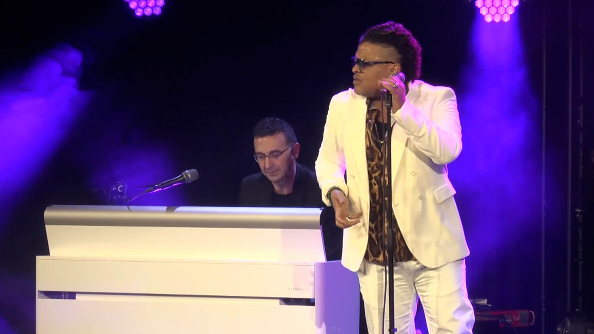 A singer performing on stage with a keyboard player under purple lights
